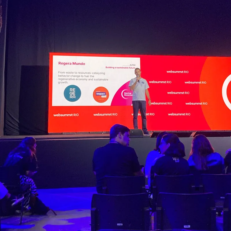 Palestrante no palco do Web Summit Rio, com o slide da Regera Mundo no telão